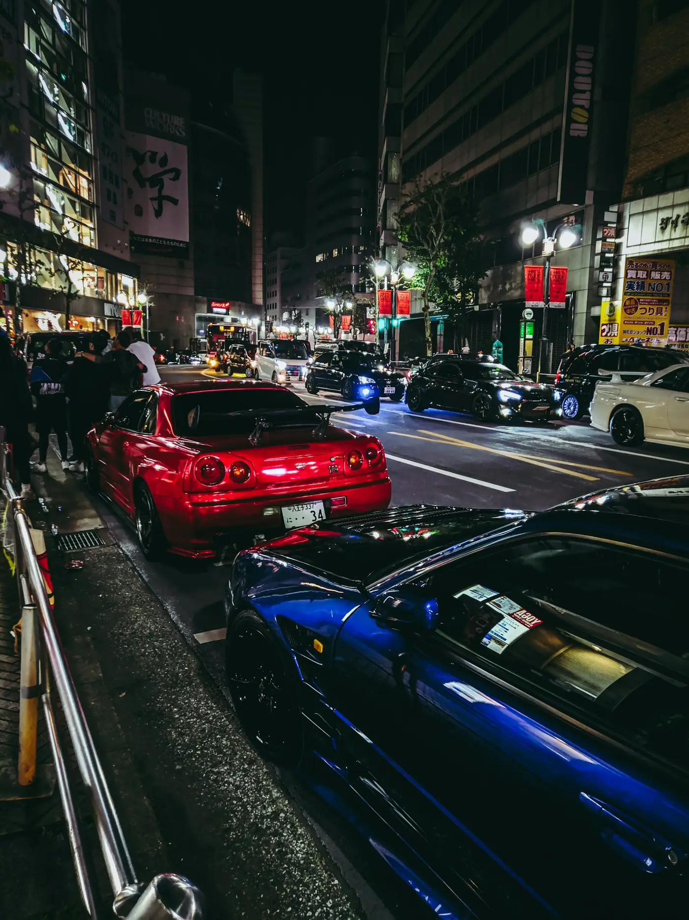 Sports cars parked along a city street at night during an enthusiast meet