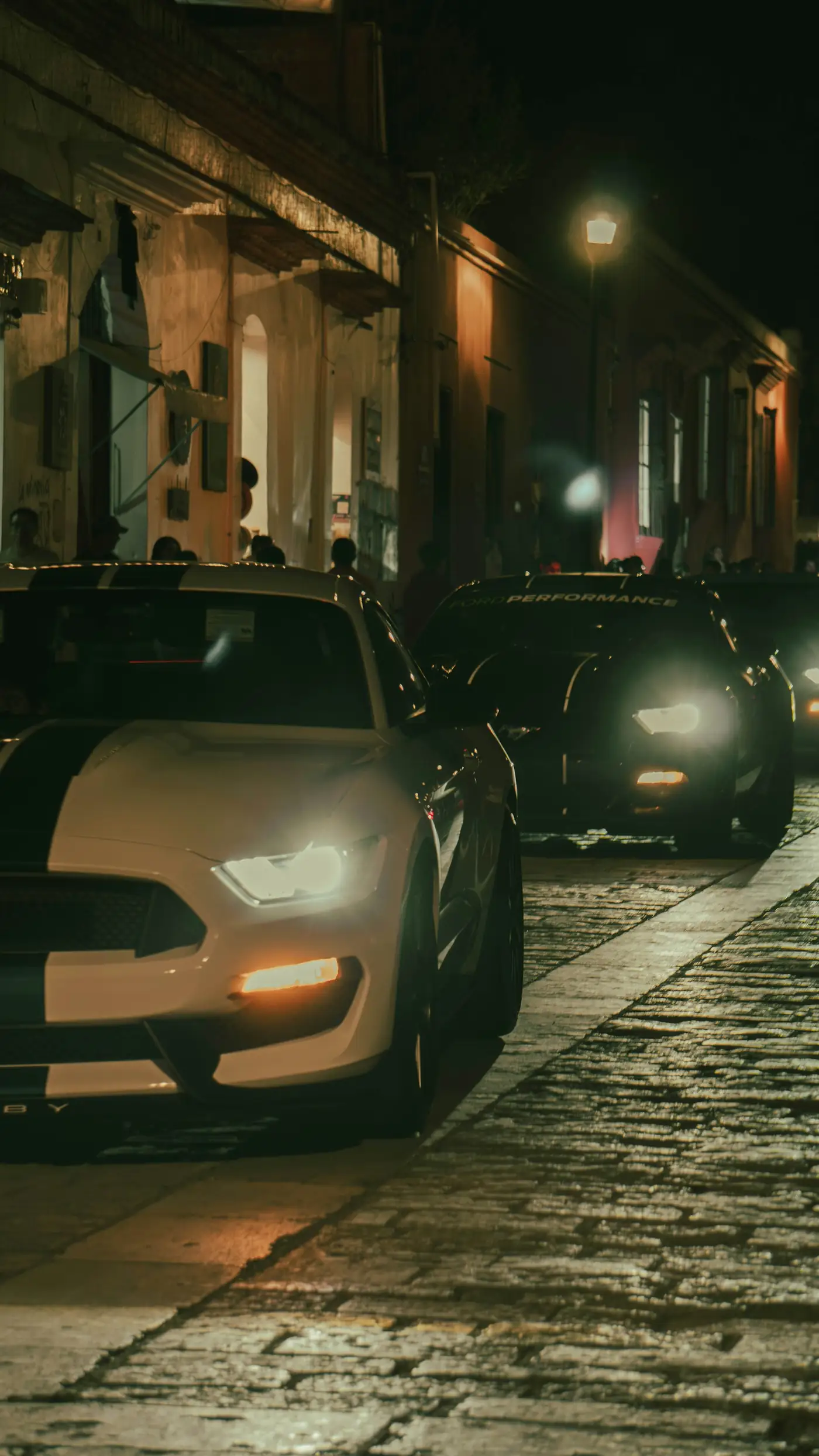 Two cars facing each other with headlights on in a dark parking area